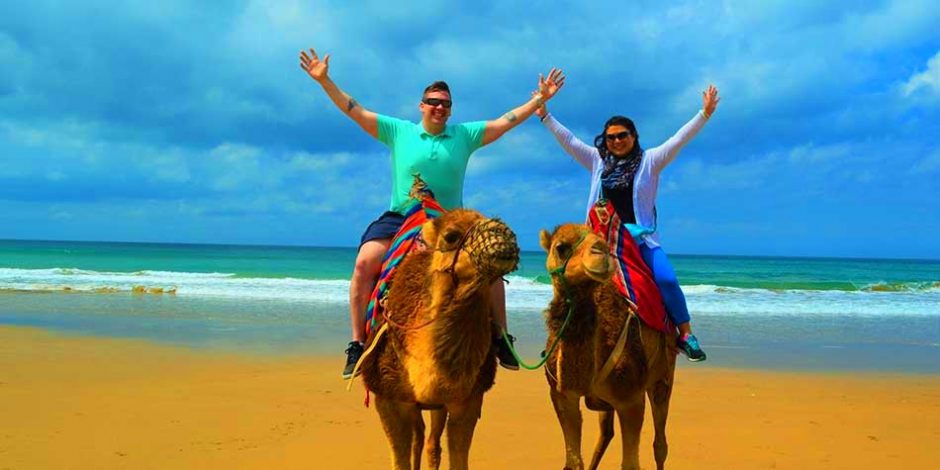 couple riding camels in tangier beach