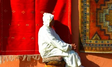 Moroccan man sitting near hanged rugs, Morocco Tour,