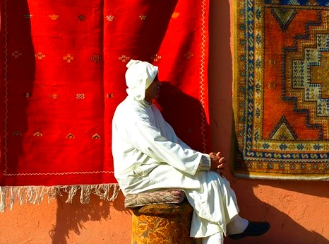 Moroccan man sitting near hanged rugs